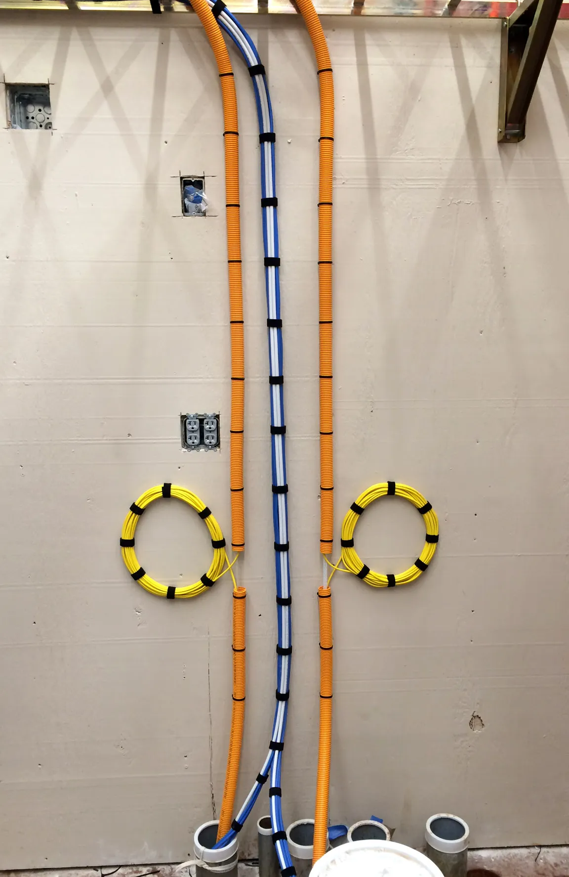 Conduit and coiled fiber optic cable runs installed on an unfinished wall with electrical outlet cutouts