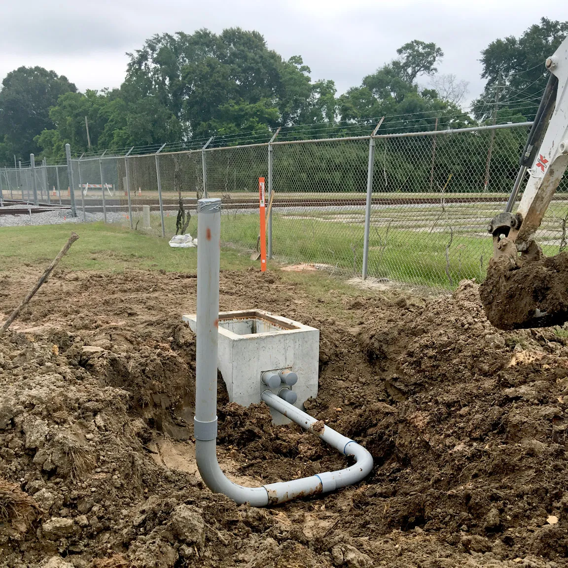 Precast concrete pull box and conduit installed in an excavated trench along a fence line