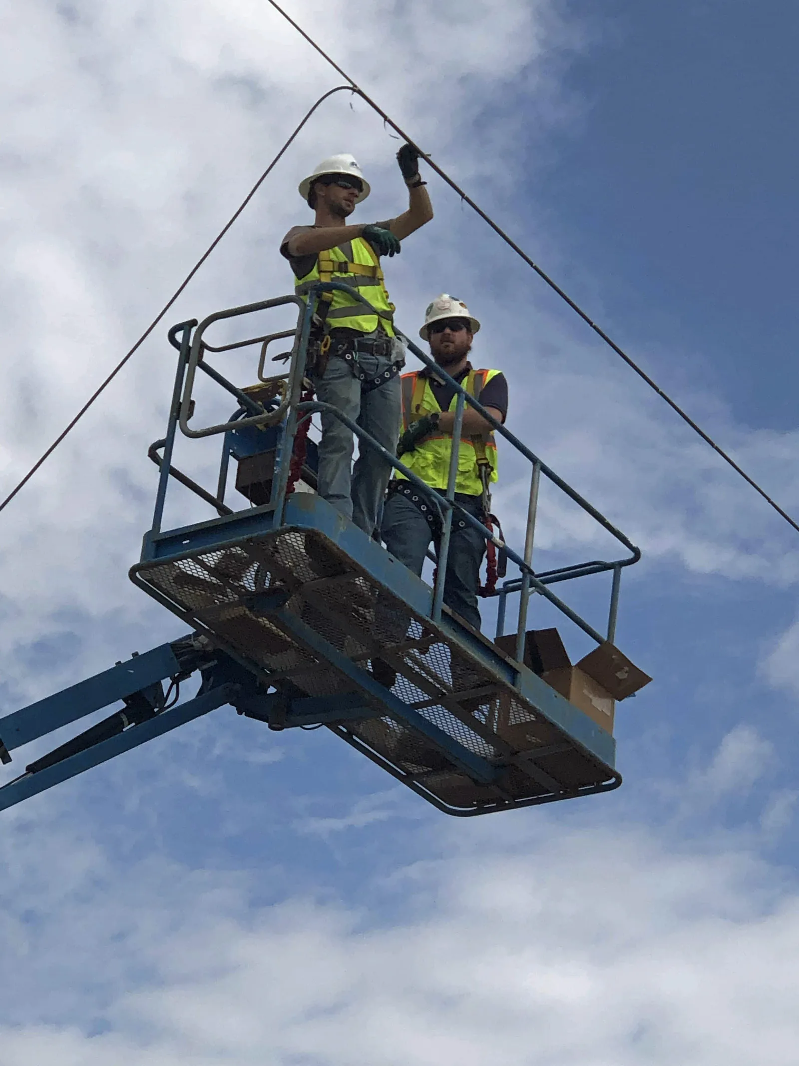 Two technicians working from an aerial lift bucket on overhead lines