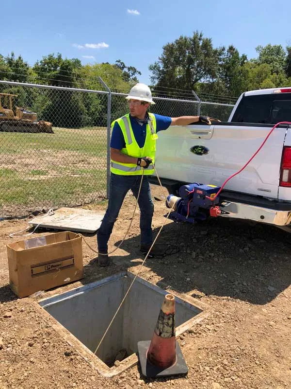 Technician using a cable-pulling winch at an open underground vault