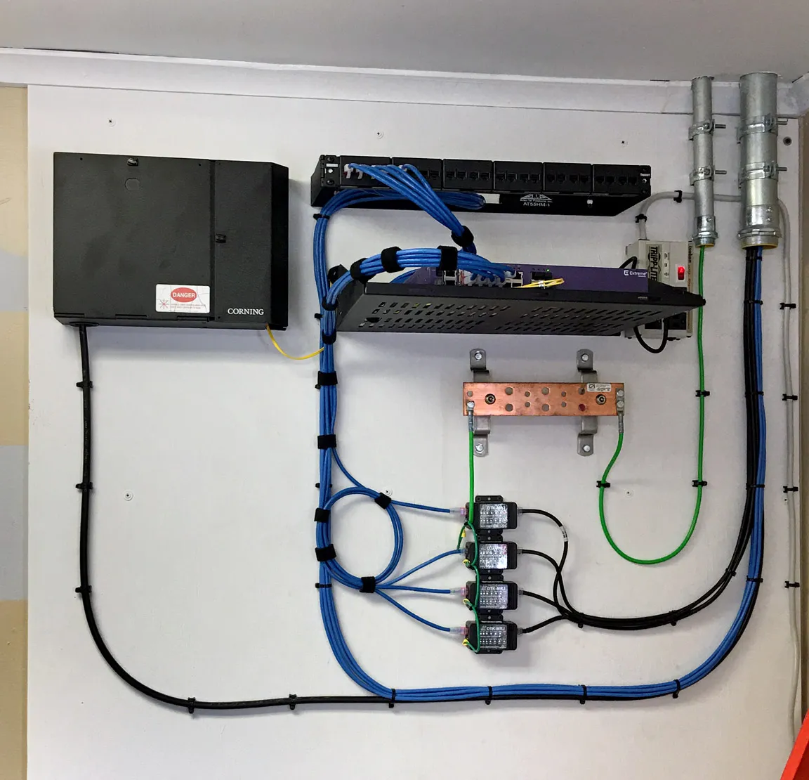 Wall-mounted communication room equipment including a fiber enclosure, patch panel, network switch, and grounding bar