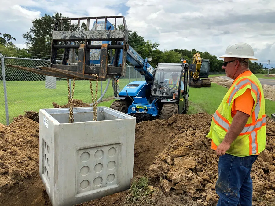 Precast concrete utility vault being lowered into a trench by a telehandler