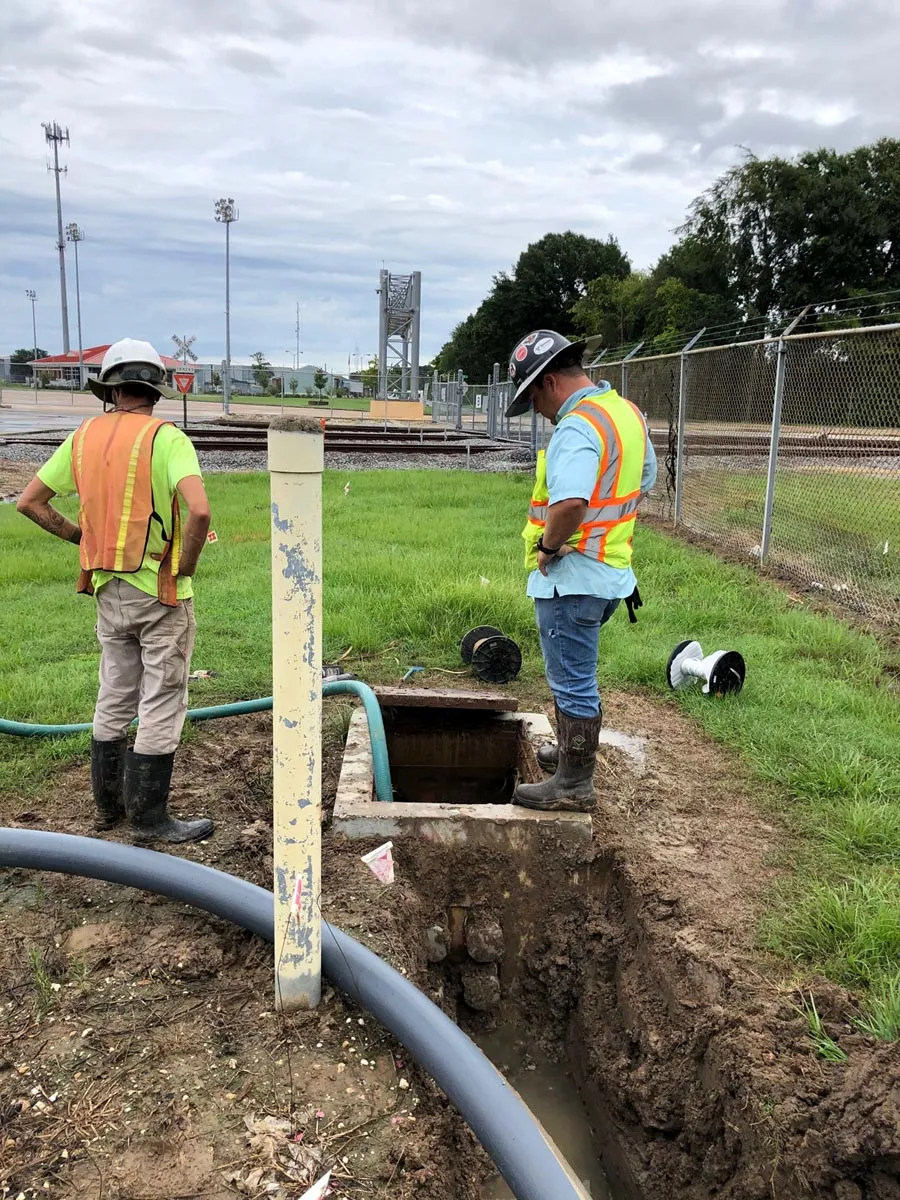 Two technicians inspecting an open underground vault near railroad tracks