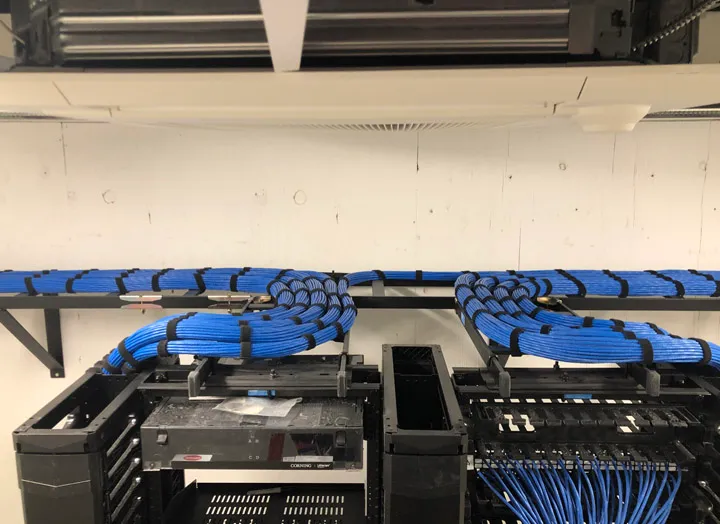 Blue network cable bundles running along an overhead tray into equipment racks