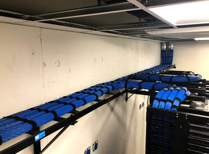 Overhead cable ladder rack routing bundled network cables along an unfinished communication room wall