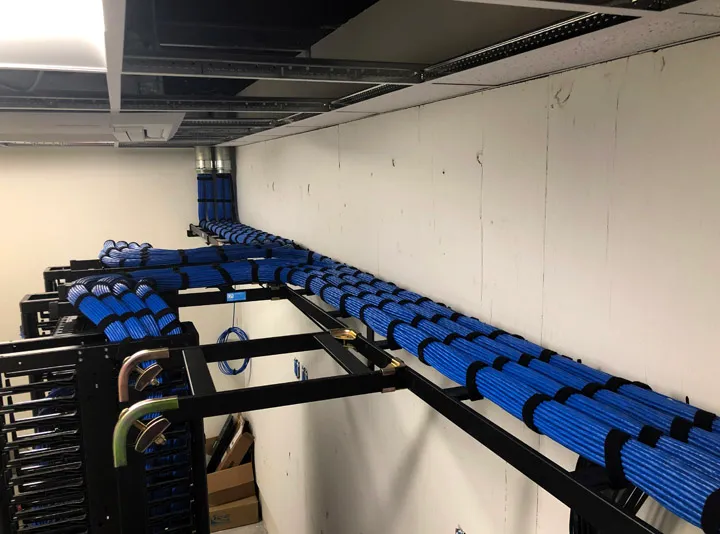 Blue network cable bundles running along an overhead cable tray toward equipment racks