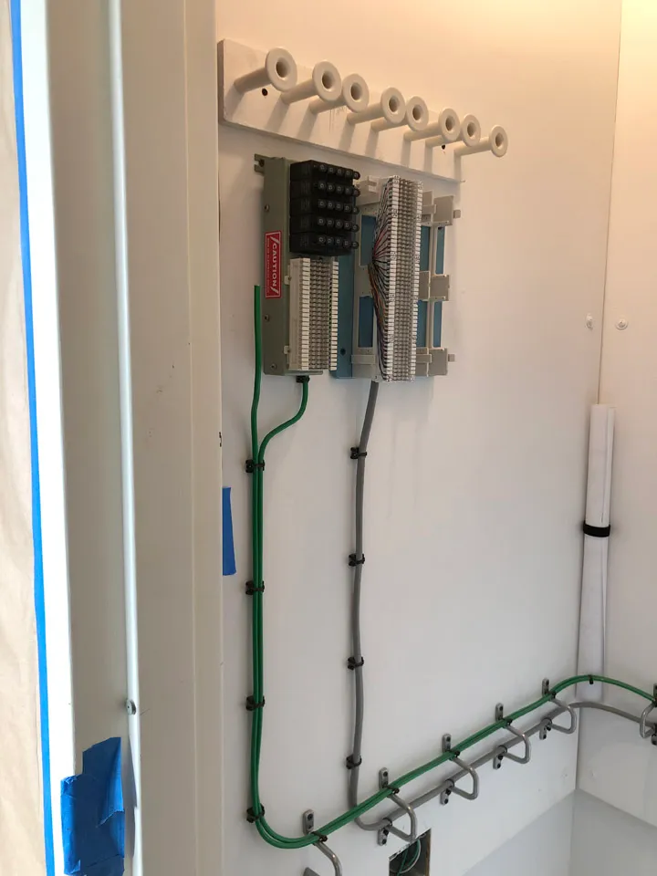 Wall-mounted punch-down terminal block with cables routed down the wall in a communication closet
