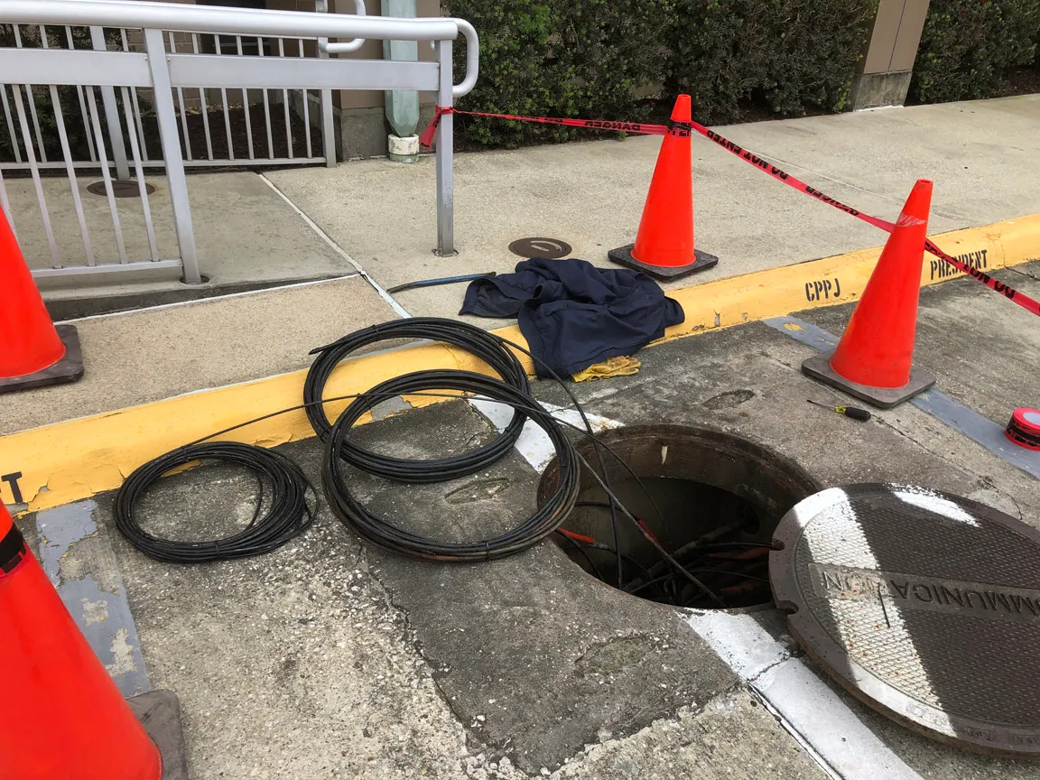 Open underground communication vault with coiled cable and traffic cones marking the work area