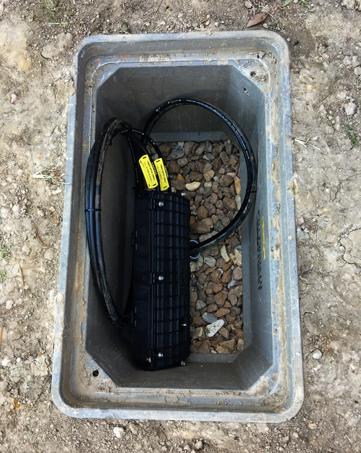 Underground fiber optic splice closure in a below-grade vault, marked with caution tags