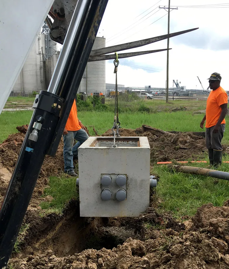 Technicians guiding a precast concrete vault into the ground near grain silos