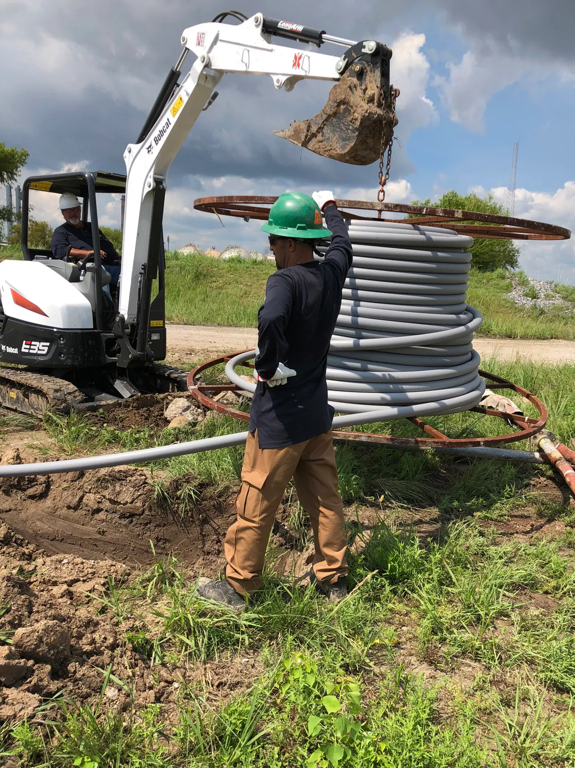 Technician pulling conduit from a reel with an excavator positioned overhead