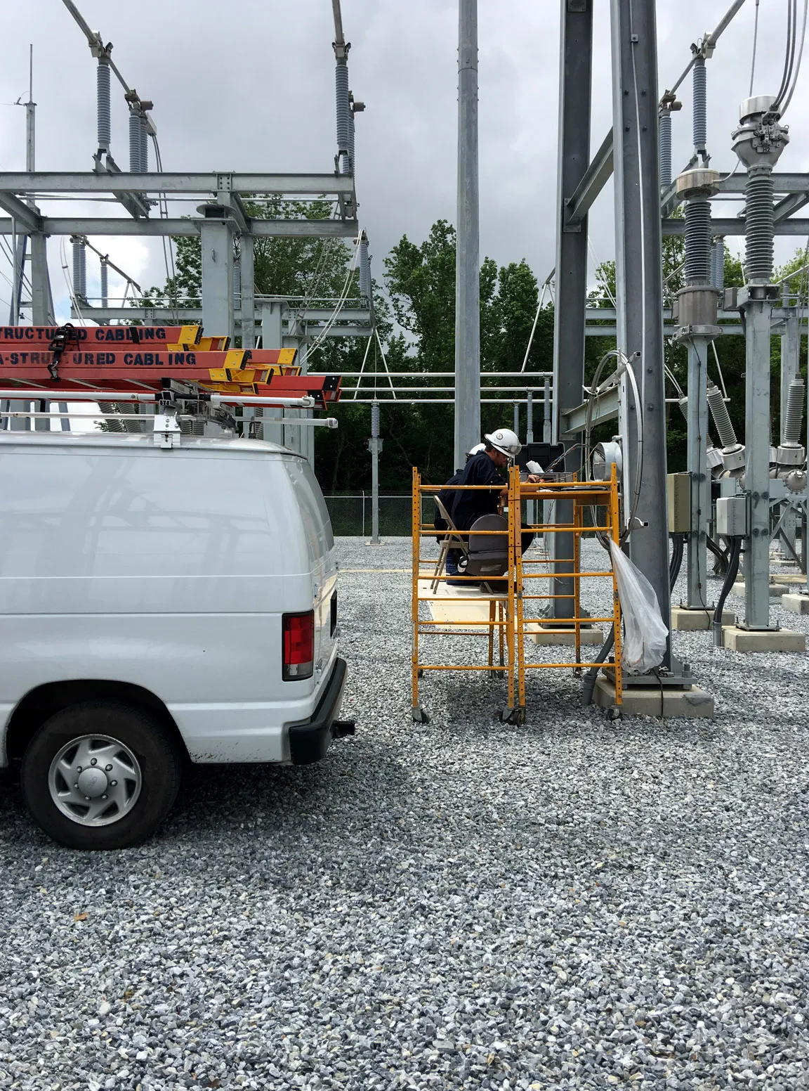 Technician working from a scaffold platform at an electrical substation next to a Louisiana Structured Cabling service van
